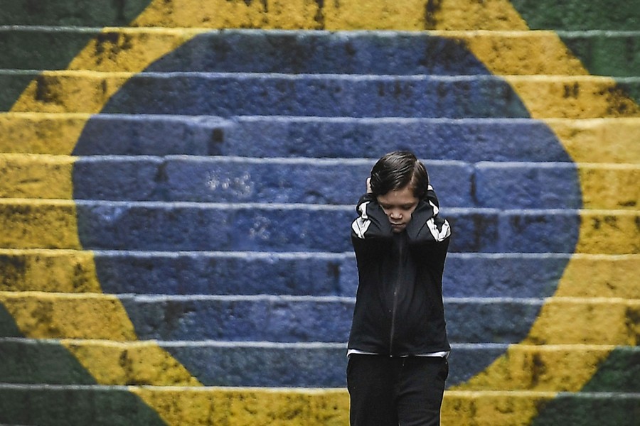 A child holds his hands over his ears, standing near a stairway painted in green, yellow, and blue.