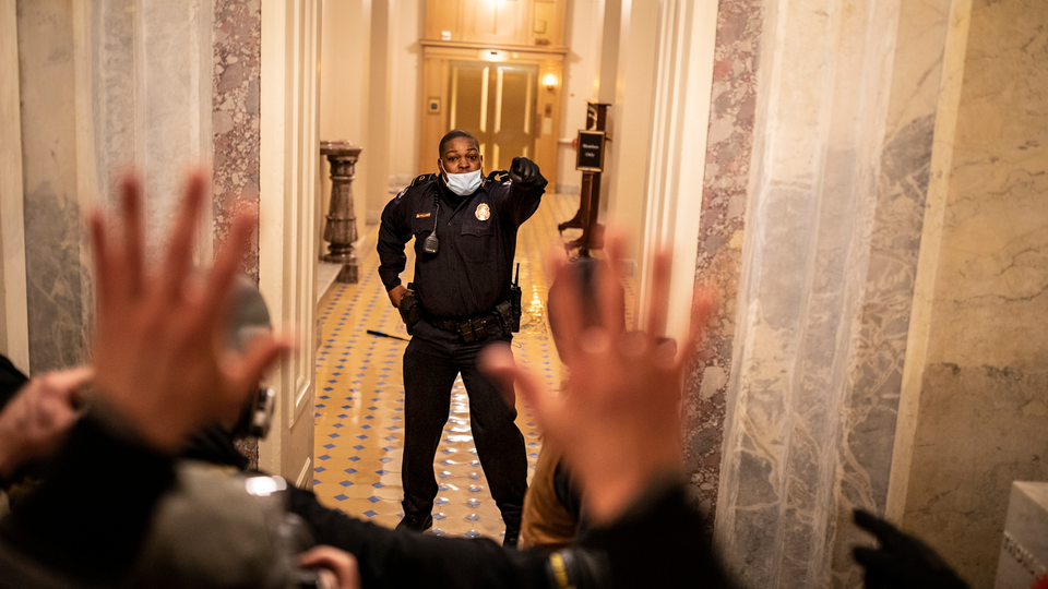 Foto del agente de policía del Capitolio Eugene Goodman parado en la entrada de las escaleras del edificio del Capitolio el 6 de enero de 2021, con la mano levantada, frente a una multitud de alborotadores.