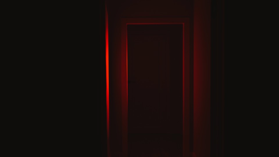Front view of a door illuminated with red lighting in dark corridor.