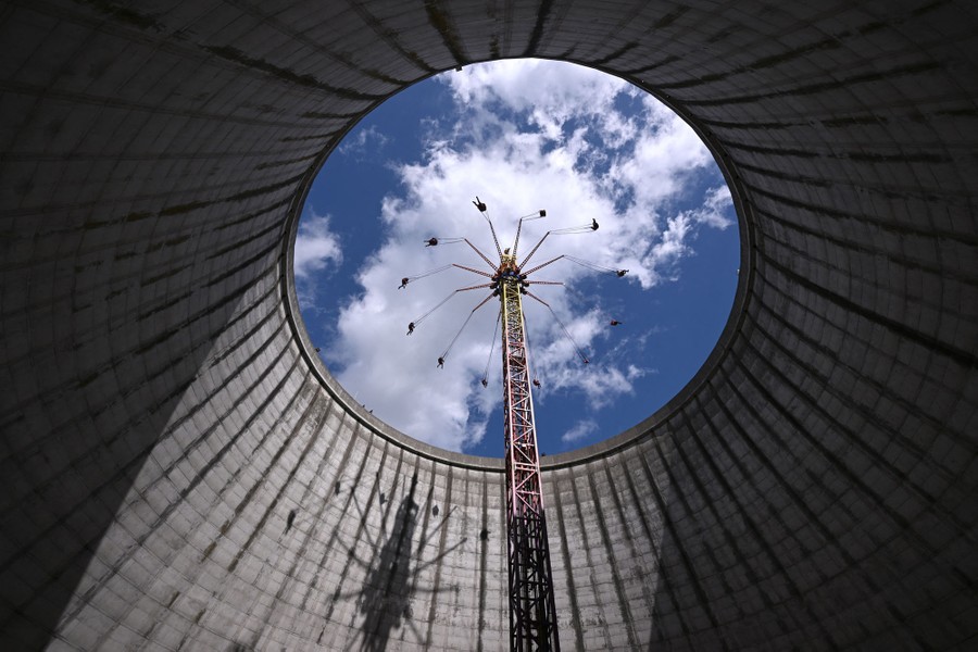 A view of an amusement ride spinning people high in the air inside an empty cooling tower.