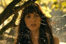 Dakota Johnson in “Madame Web,” standing in front of a spider web while backlit by the sun