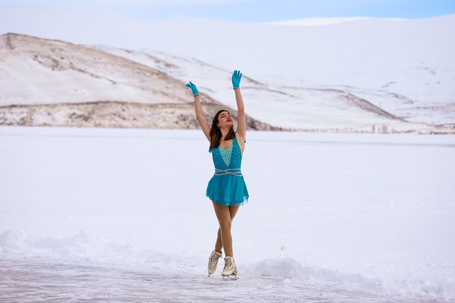 A figure skater in costume performs on a frozen lake in the mountains.