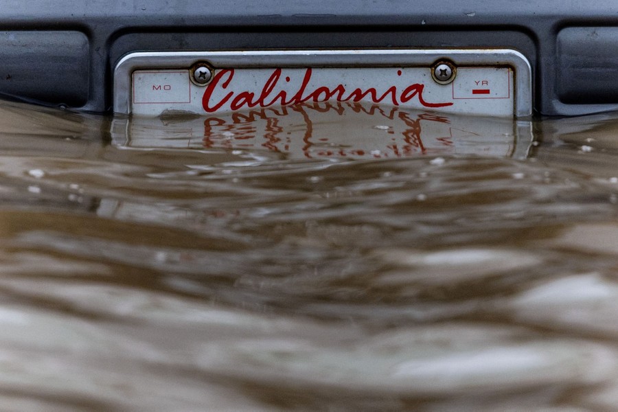 A license plate on a car bumper is partially submerged in floodwater.