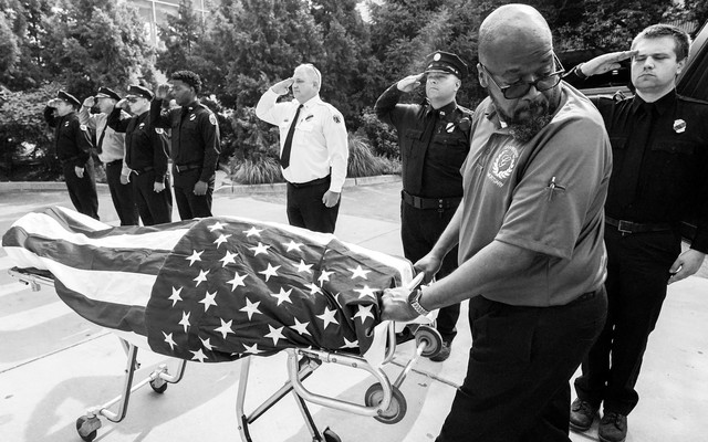 A man wheels the flag-covered body of a firefighter who died of COVID-19 past saluting officers.