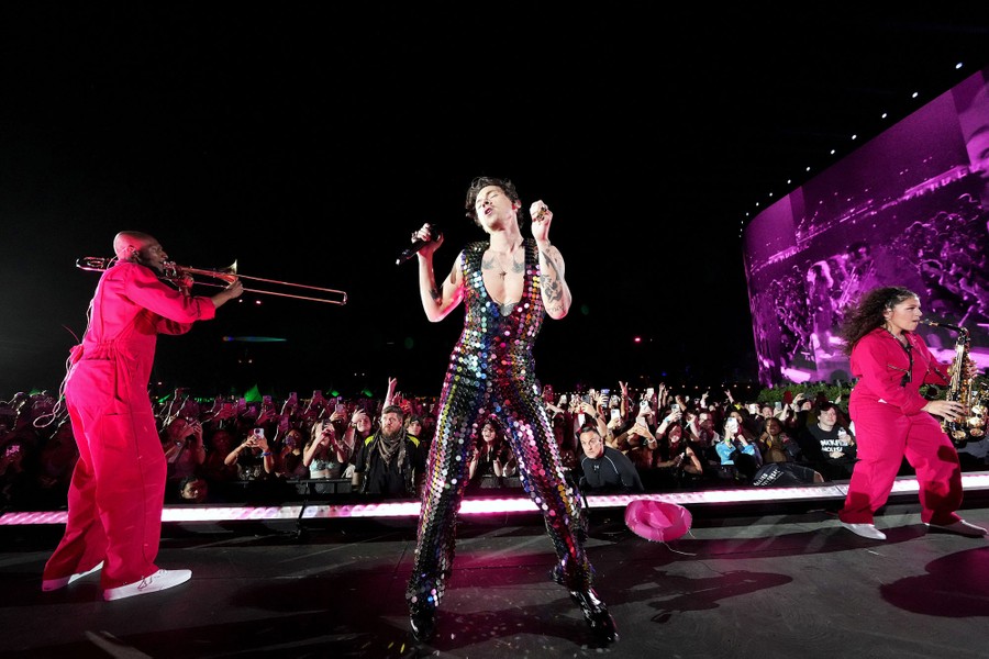 Performer Harry Styles dances on a stage with a large crowd watching below.