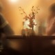 A blurry image of two people seated at a warmly lit table, a vase of flowers between them
