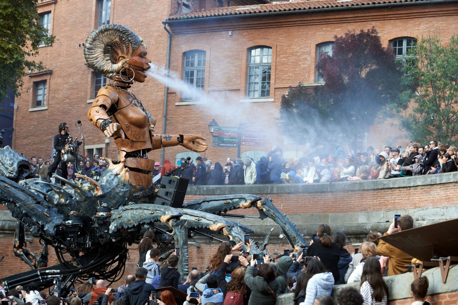 A giant puppet sprays water from its mouth onto a crowd below.