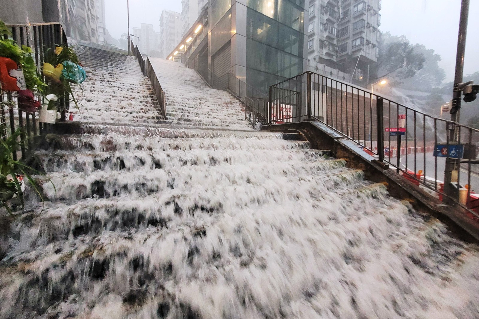 Floodwater flows down a wide public staircase during a rain storm.