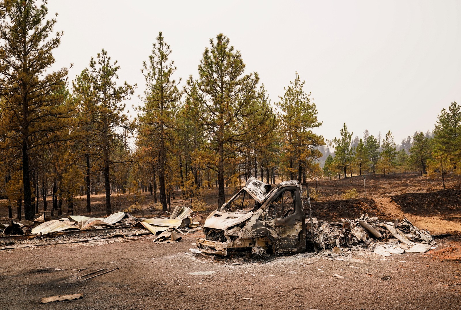 A charred vehicle lies on the side of a road after a fire.