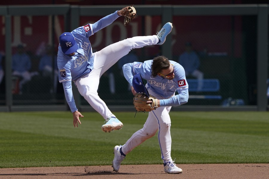 A baseball player leaps over a teammate, allowing him to field a ball.