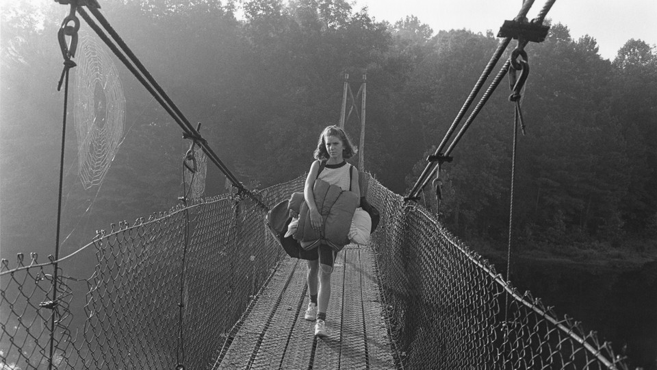 A girl carrying a sleeping bag walking over bridge