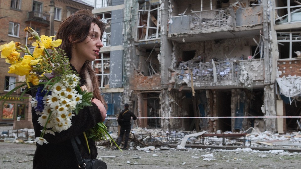 A woman holding flowers walks by the rubble of a bombed out apartment building