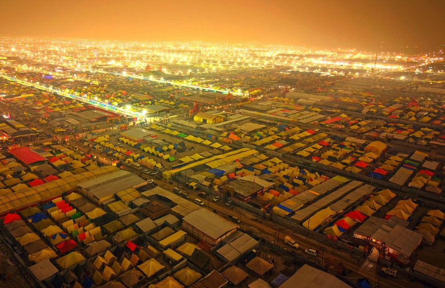 An aerial view of a vast tent encampment set up as a grid, lit by street lamps
