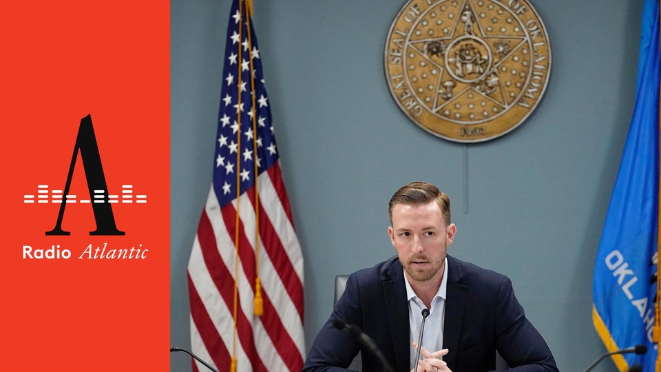 Oklahoma State Superintendent Ryan Walters sits at a table with an American flag and the state flag of Oklahoma.