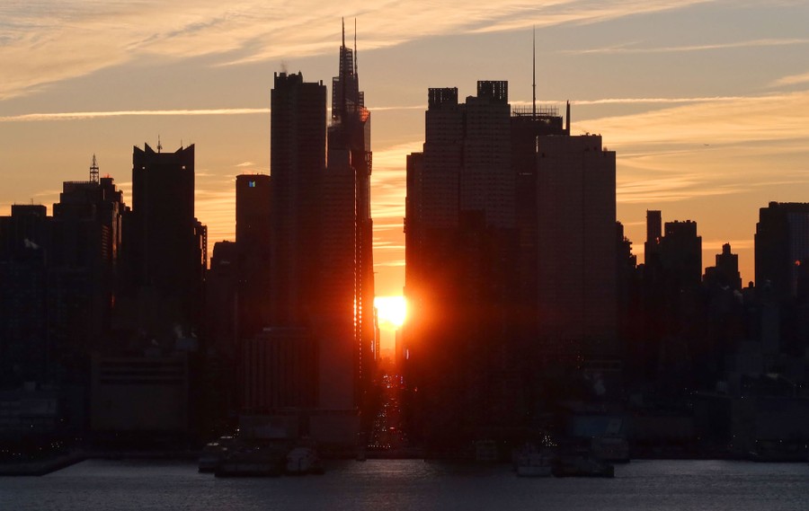 A sunrise is viewed between tall skyscrapers of Manhattan.