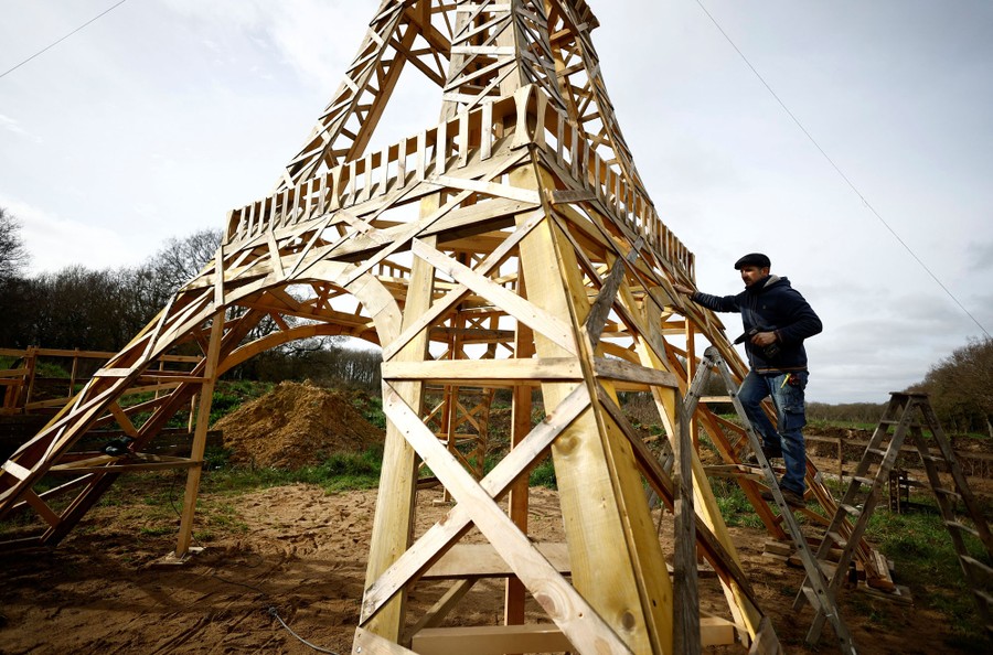A person works beside a wooden replica of the Eiffel Tower.
