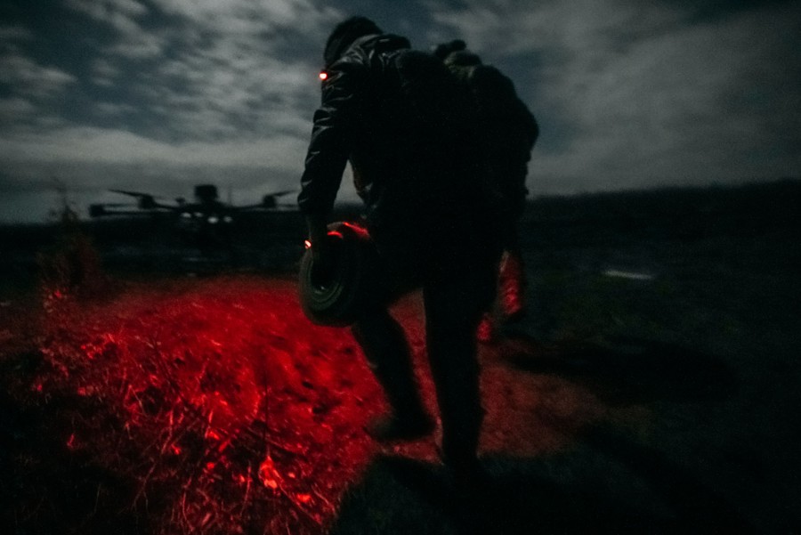 A night view of a soldier running through a field, lit by a red light strapped to their head.