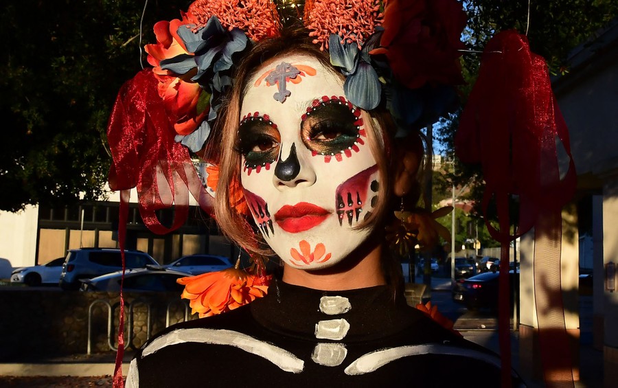 A person stands outside wearing ornamental skull makeup and a floral headdress.