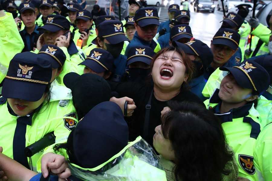 A person yells while being restrained by a large number of police officers during a protest.