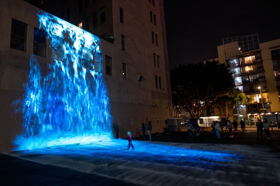 People walk near a lightshow projected on a downtown building.