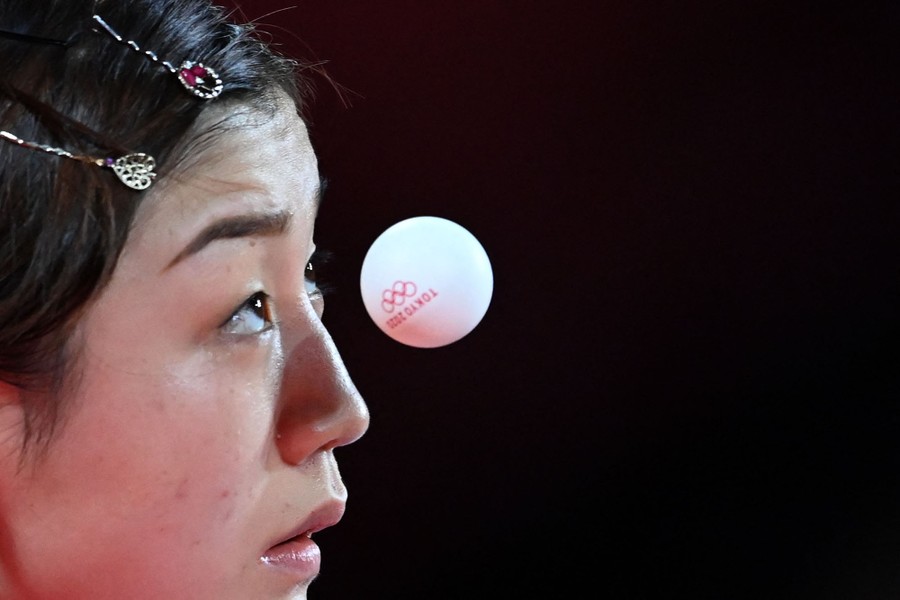 A table-tennis player eyes a ball very close to her face.
