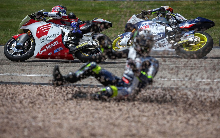 A motorcycle racer slides chaotically through gravel beside a track as other riders drive past.