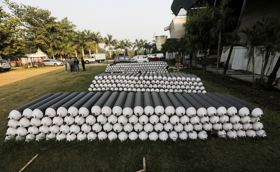 Hundreds of oxygen cylinders are seen stacked in a yard.