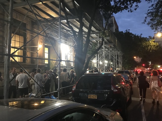 A bunch of people standing in line outside in Manhattan at nighttime.