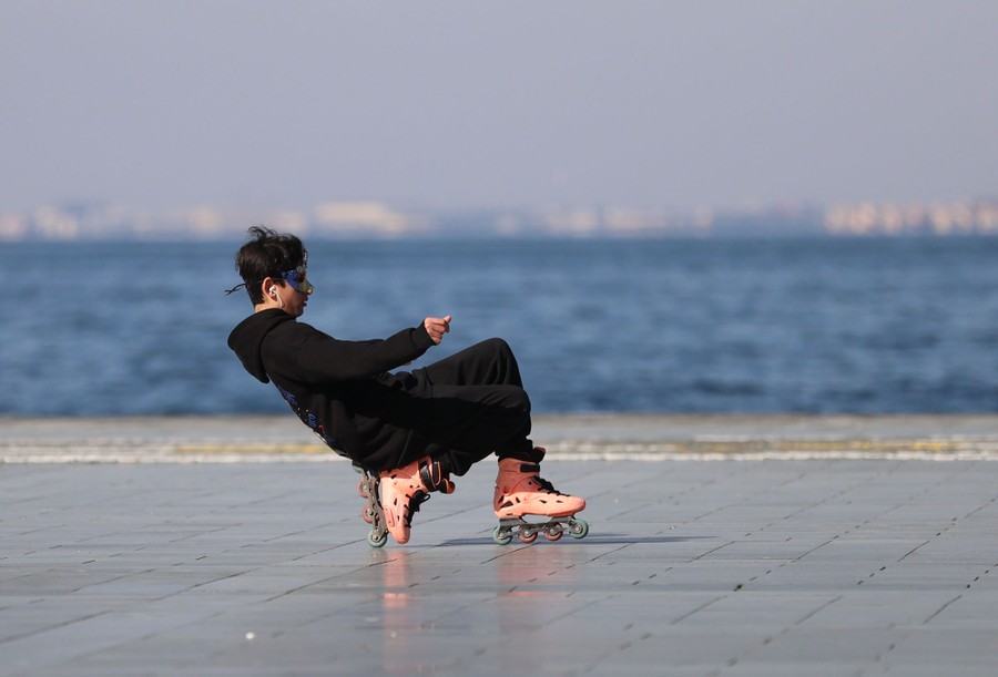 A person rollerblades on a plaza near a shoreline.
