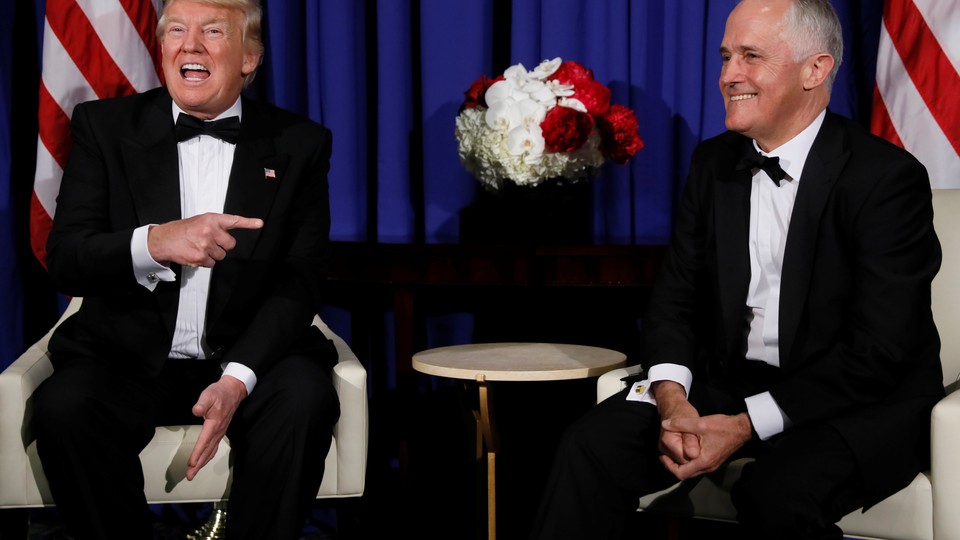 President Donald Trump and Australian Prime Minister Malcolm Turnbull sit on chairs and laugh.