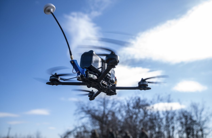 A small four-rotor drone, in flight, carrying an unidentified payload