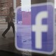 People walk past a Facebook logo on a shop window