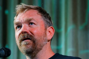 Photograph of Graham Platner speaking into a microphone against a blue-green backdrop