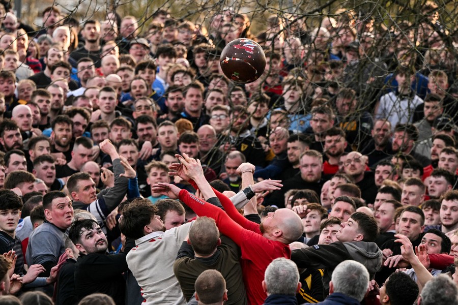 A large crowd of almost all men watches as other men smash together, trying to get possession of a ball in midair.