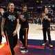 Photograph of WNBA athletes on a court wearing T-shirts that read “Pay Us What You Owe Us”