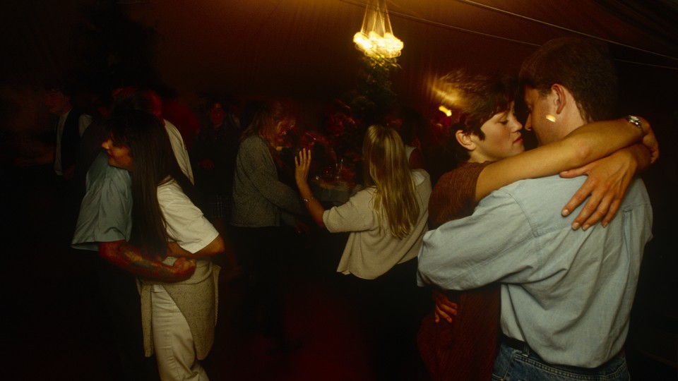 Couples dance closely in a dimly lit room.