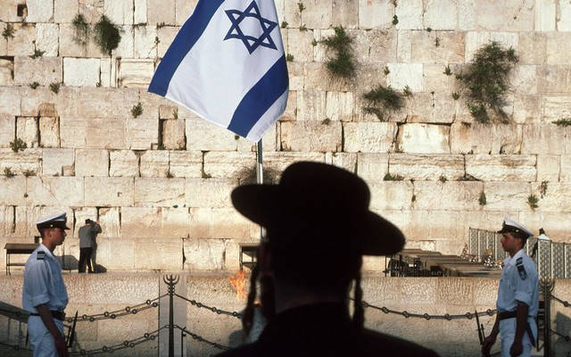 A photograph of the Wailing Wall with an Israeli flag and two guards.