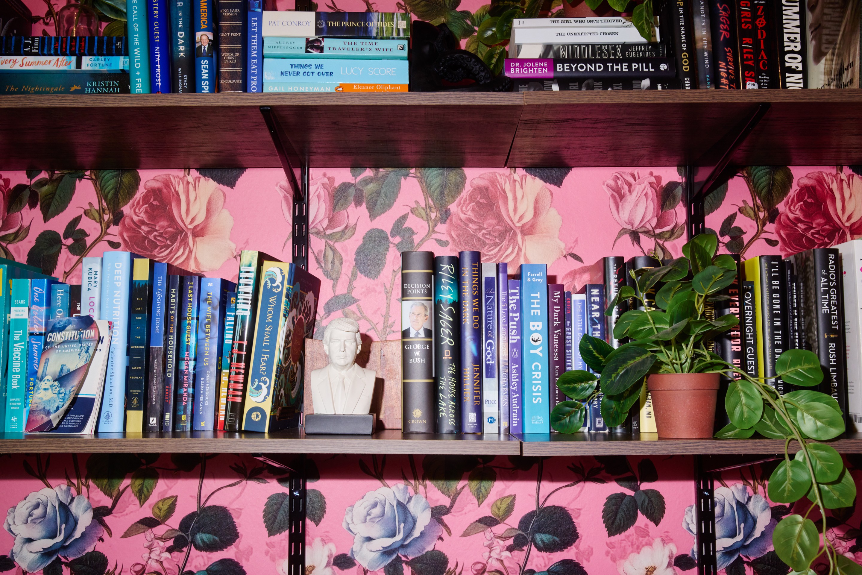 books on a book shelf in front of flower wallpaper