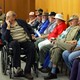 Older people wait in chairs and wheelchairs.