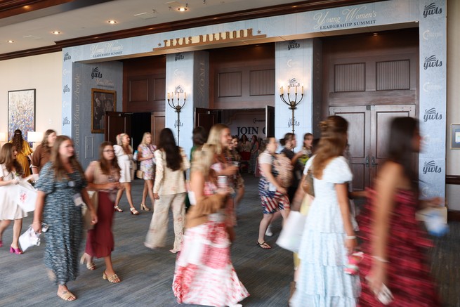 A color photograph of women in long dresses walking in a convention center