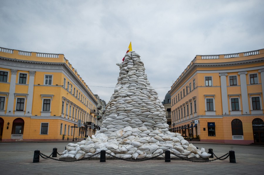 A tall monument in a square is covered with a pile of sandbags.