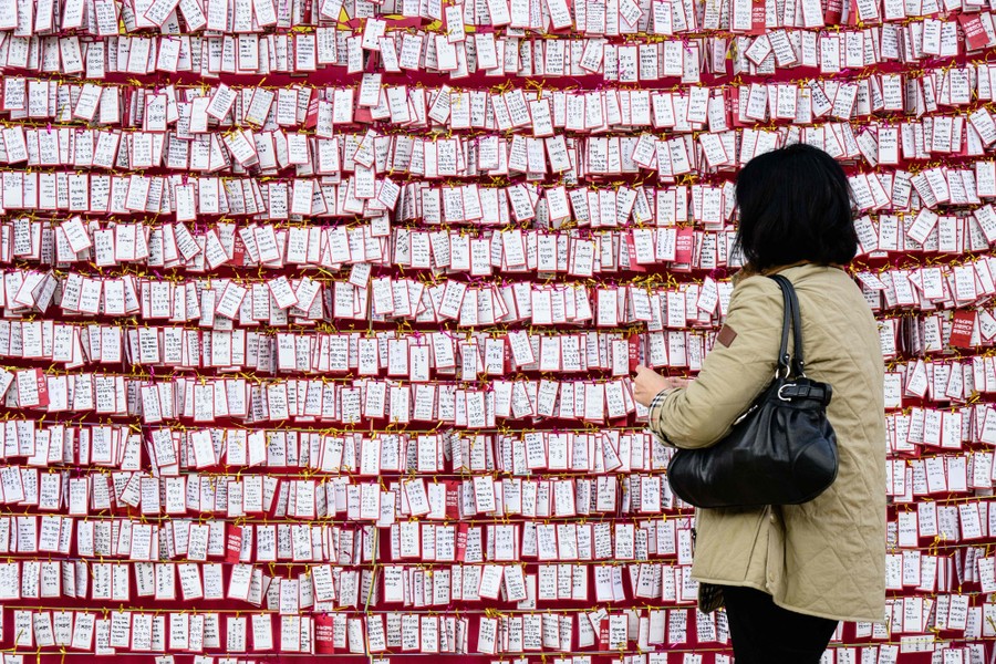 A person hangs a small note on a wall where hundreds of other notes have already been placed.