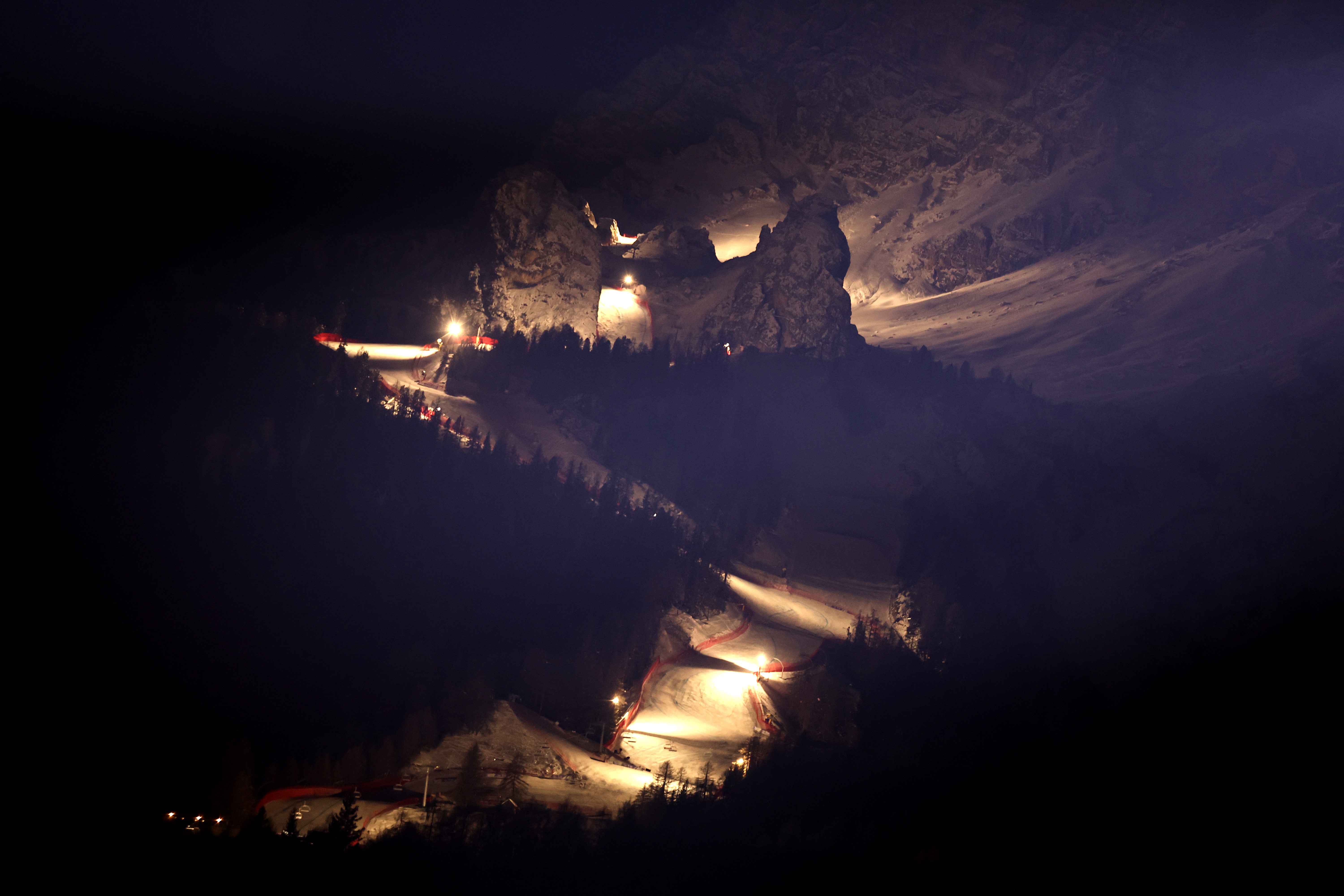 A night view of an Alpine ski run, lit by floodlights on the course.