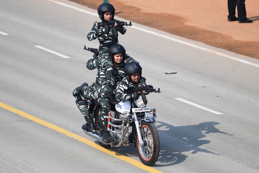Four soldiers, stacked on top of one another, ride a motorcycle, as three of them hold weapons.