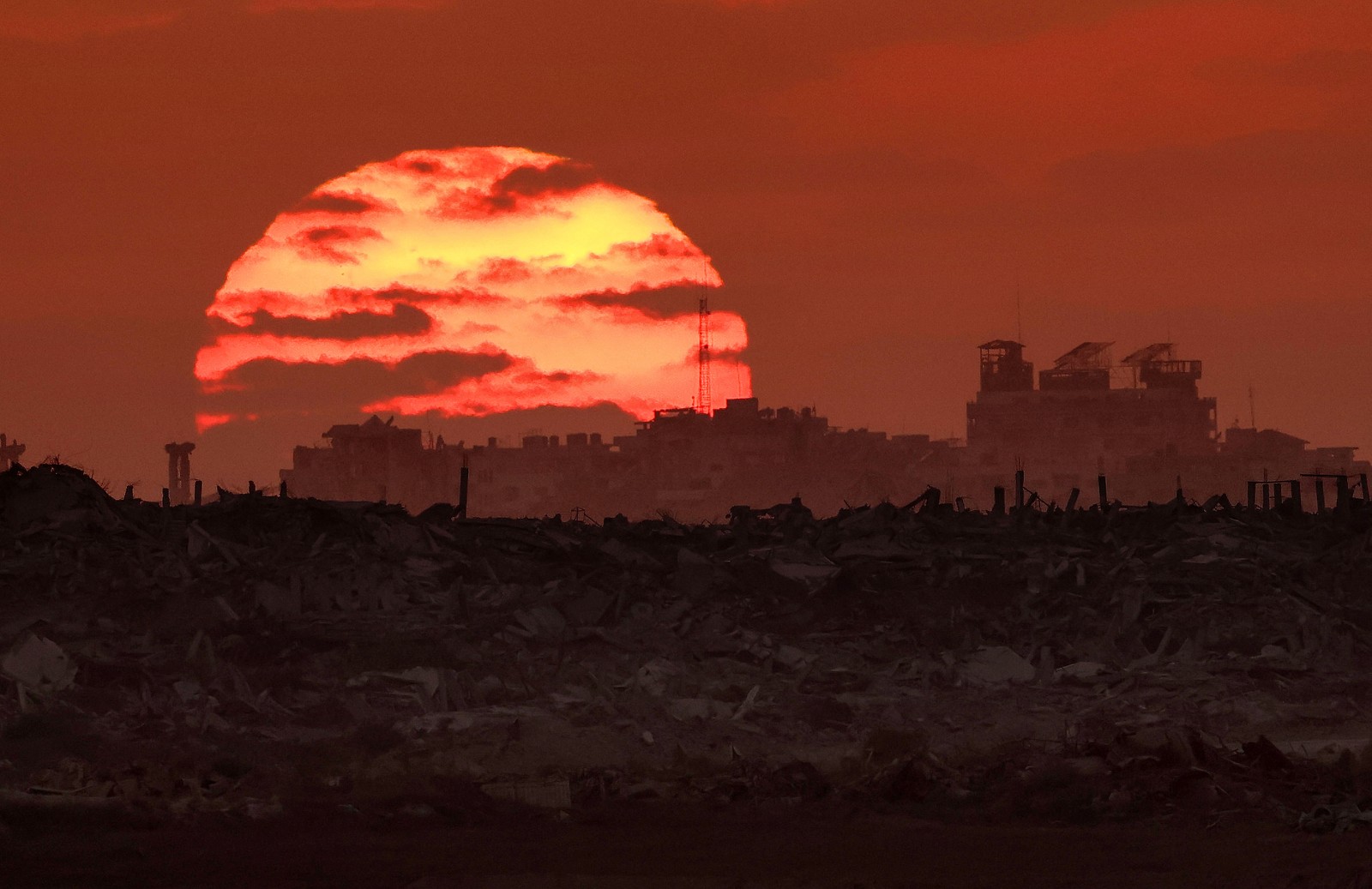 Clouds partially obscure a sunset over ruined buildings in Gaza.