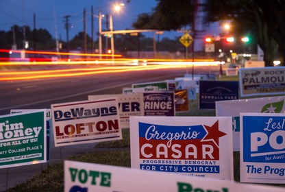 Political signs crowded together against the side of a road at night.