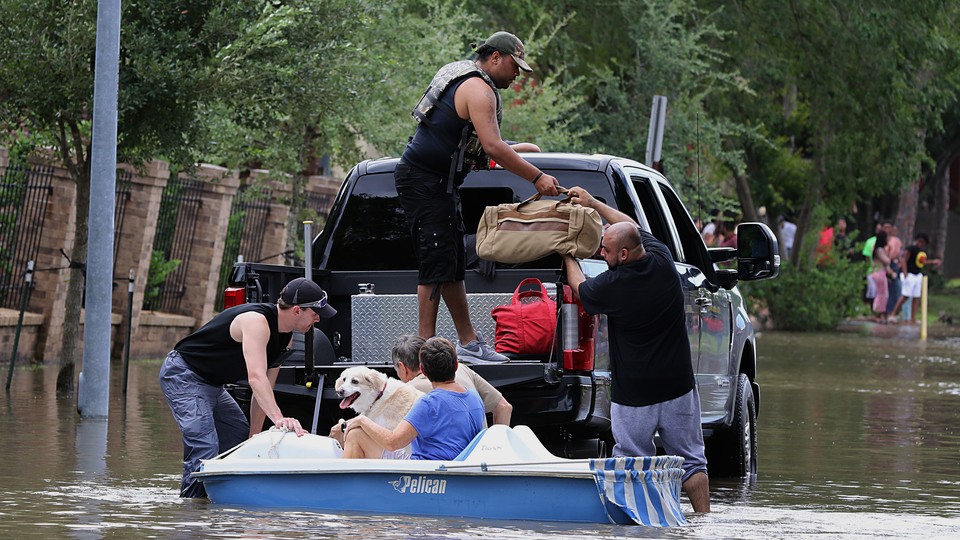 Five people load up duffel bags and a dog onto a truck bed in a flooded street.