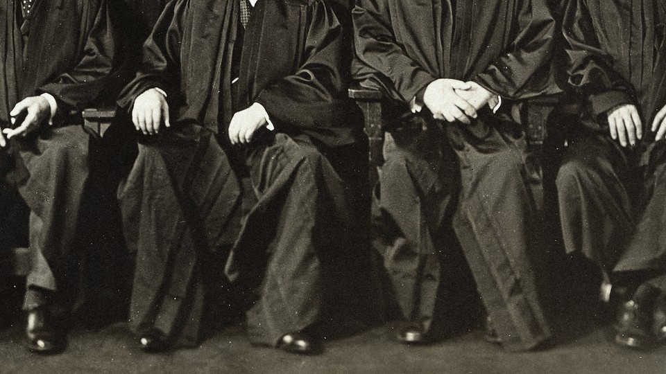A black and white photo of four light skinned men in robes, their heads not visible