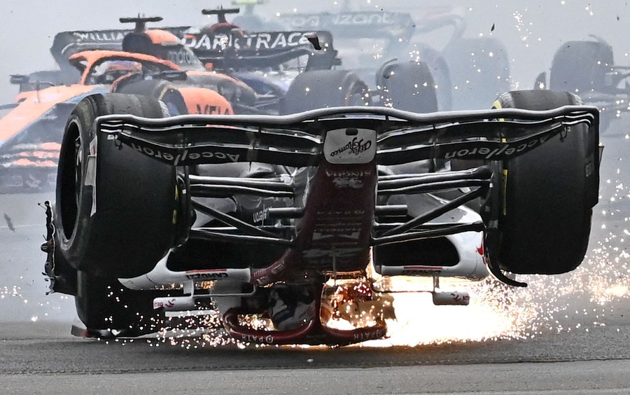 An F1 race car skids upside down, throwing sparks, as other cars pass behind it.