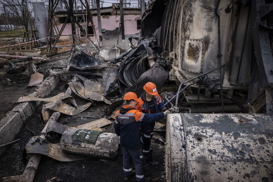 Workers stand beside large electrical equipment that has been destroyed.